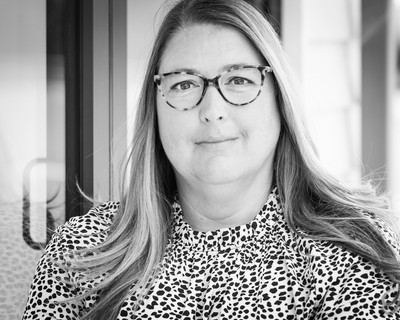 Professional headshot photograph in black and white of a female wear glasses, shot against an environmental background
